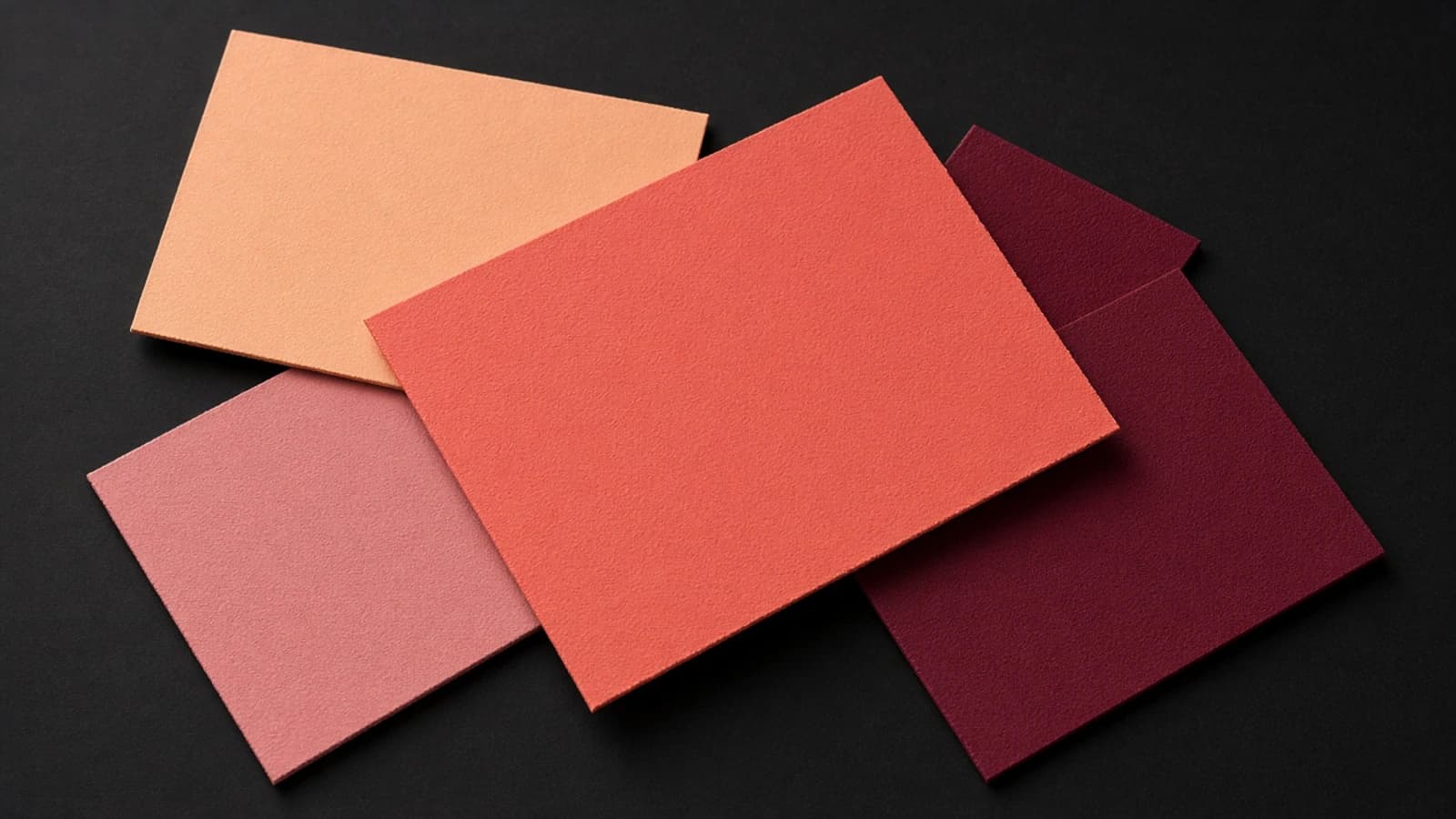 Four overlapping paper swatches on black: peach, rose, a large coral red, and burgundy.